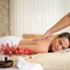Une femme détendue reçoit un massage du dos, avec des orchidées roses et des huiles de massage à proximité. Offrez-vous un abonnement massage pour un bien-être continu.