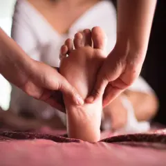 Mains massant un pied, offrant détente et bien-être à l'ensemble du corps.