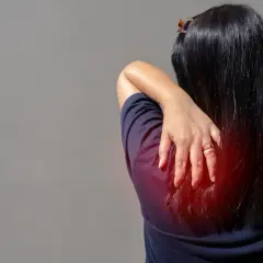 Douleur au muscle omoplate, une main masse la zone rouge sur le dos d'une femme.