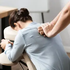 Un masseur offre des massages en entreprise à une femme assise sur une chaise ergonomique, soulageant les tensions du dos.