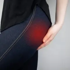 Une main touche la hanche, une zone rouge indiquant une douleur liée au syndrome fessier profond.