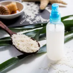 Bouteille de spray remplie d'eau de riz, avec une cuillère de riz et du miel en arrière-plan.