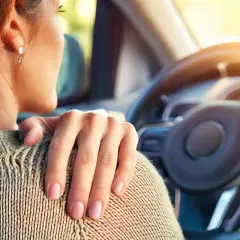 Femme au volant, main sur l'épaule, souffrant de tendinite. La conduite de voiture peut être douloureuse.
