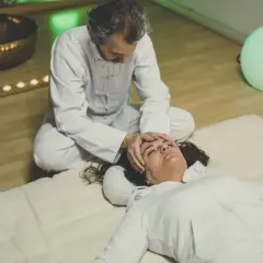 Un praticien effectue un massage japonais shiatsu sur le visage d'une femme allongée, dans une ambiance apaisante avec une lumière verte et des bougies.