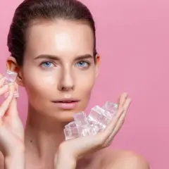 Une femme au visage frais tient des glaçons dans ses mains, un geste rafraîchissant pour la peau.