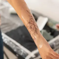 Application d'une crème sur un tatouage floral pour favoriser la cicatrisation. La peau est légèrement brillante.