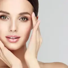 Visage de femme aux mains délicates caressant sa peau, évoquant un soin de nettoyage de peau parfait.