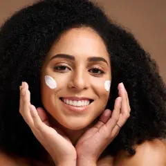 Une femme souriante avec des touches de crème sur les joues, profitant des bienfaits du beurre de karité visage pour une peau douce et hydratée.