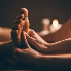 Mains massant un pied, éclairé par des bougies. Une invitation à découvrir ce qu'est la réflexologie plantaire.