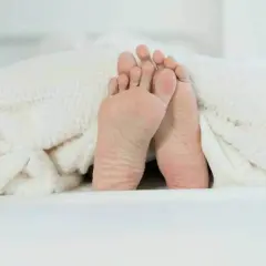 Pieds sous une couverture douillette, prêts pour un point massage pied pour dormir paisiblement.