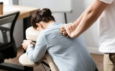 Un masseur offre des massages en entreprise à une femme assise sur une chaise ergonomique, soulageant les tensions du dos.