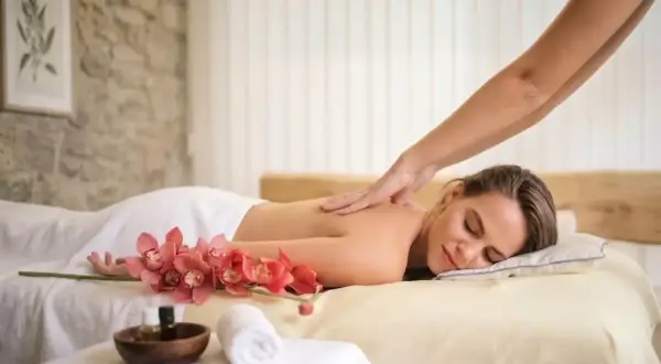 Une femme détendue reçoit un massage du dos, avec des orchidées roses et des huiles de massage à proximité. Offrez-vous un abonnement massage pour un bien-être continu.
