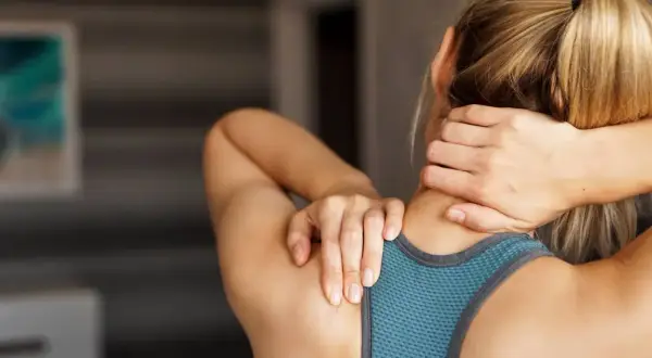 Une femme se masse le cou et les épaules, cherchant un soulagement pour ses trapezes tendus.