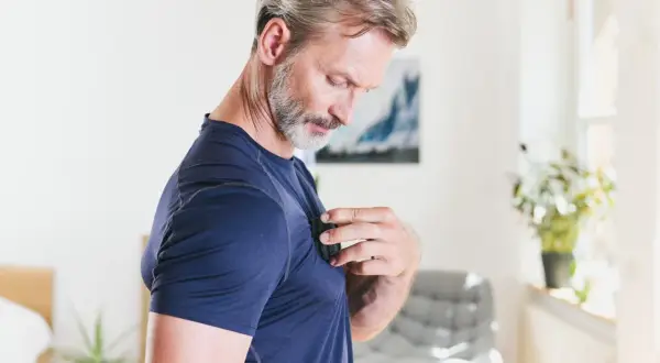 Homme d'âge mûr, torse gainé, se touche la poitrine, peut-être une contracture pectorale.