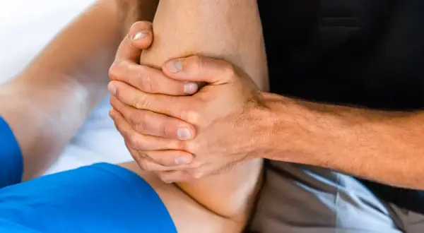 Mains expertes prodiguant un massage après sport sur une jambe. Soulagement musculaire garanti.