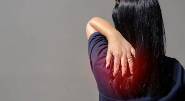Douleur au muscle omoplate, une main masse la zone rouge sur le dos d'une femme.
