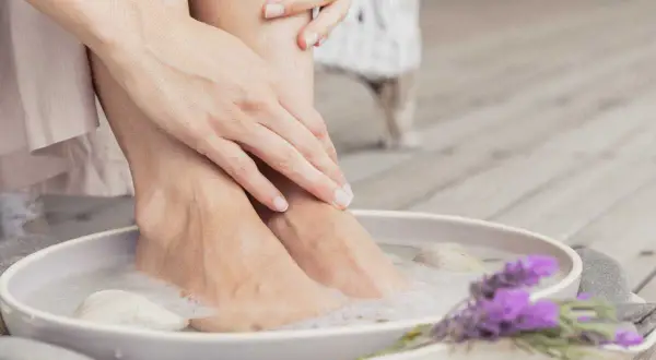 Détente avec un bain de pied maison, pieds dans l'eau savonneuse, galets et lavande.