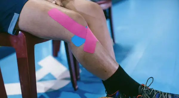Jambe d'athlète avec un strap quadriceps rose et bleu, prêt pour l'action.