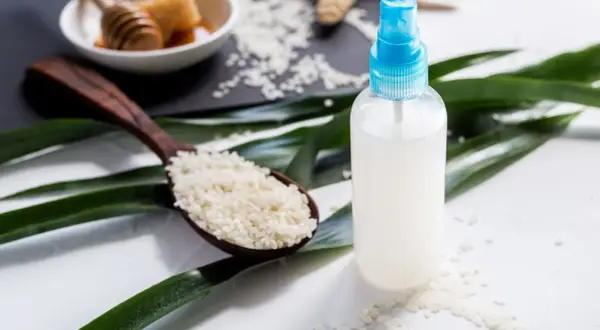 Bouteille de spray remplie d'eau de riz, avec une cuillère de riz et du miel en arrière-plan.