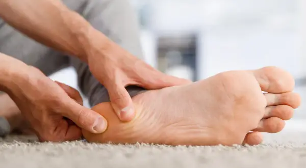 Main d'une personne massant la plante du pied pour soulager douleur.