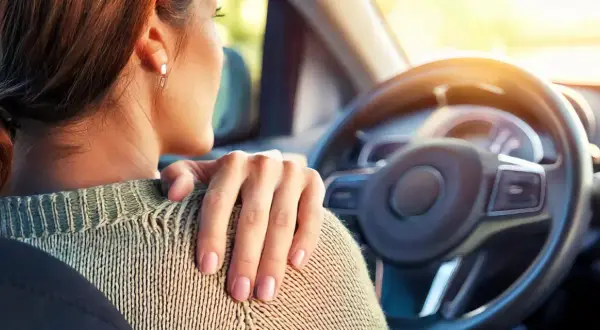 Femme au volant, main sur l'épaule, souffrant de tendinite. La conduite de voiture peut être douloureuse.