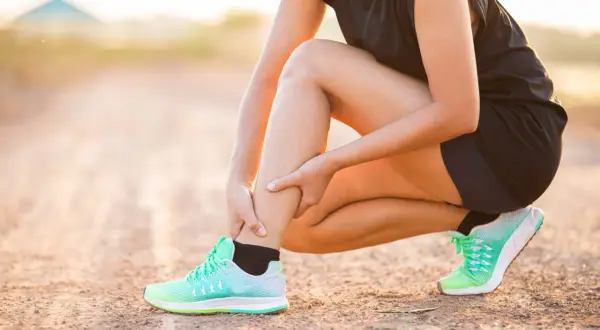 Une coureuse s'accroupit, se tenant le mollet, peut-être à cause d'une myalgie.