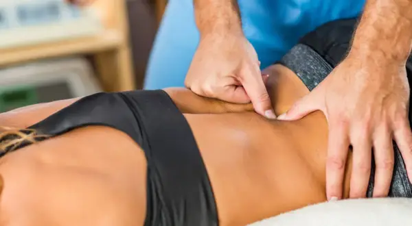 Mains d'un kinésithérapeute massant le bas du dos d'une femme, soulageant une potentielle déchirure musculaire.