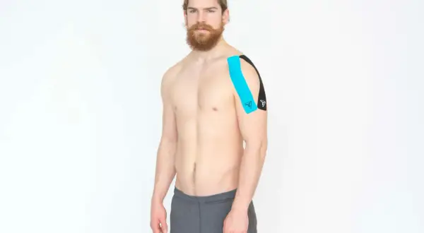 Homme avec un taping bleu et noir sur l'épaule, pour le soutien de la coiffe rotateur.