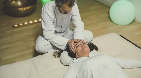 Un praticien effectue un massage japonais shiatsu sur le visage d'une femme allongée, dans une ambiance apaisante avec une lumière verte et des bougies.