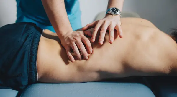 Mains d'un thérapeute massant le dos d'un patient, soulageant un muscle froissé.