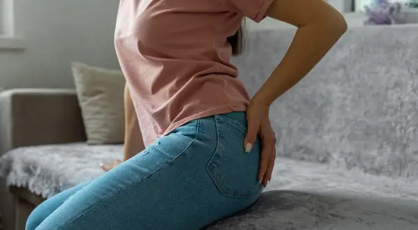 Femme assise sur un canapé, main sur la hanche, possiblement une douleur au piriforme.