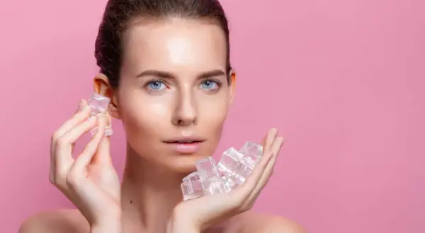 Une femme au visage frais tient des glaçons dans ses mains, un geste rafraîchissant pour la peau.