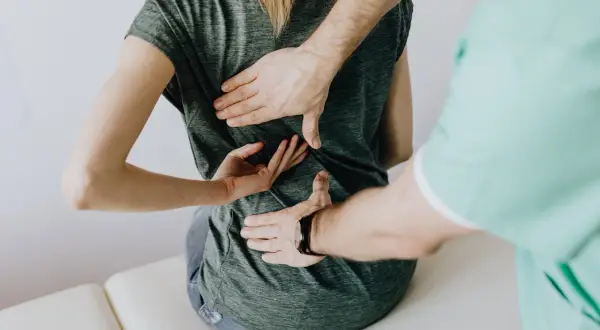 Mains d'un kinésithérapeute palpant le dos d'une patiente, cherchant à comment soulager une scoliose.