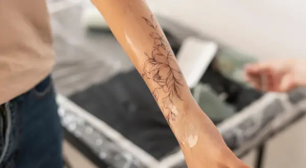 Application d'une crème sur un tatouage floral pour favoriser la cicatrisation. La peau est légèrement brillante.