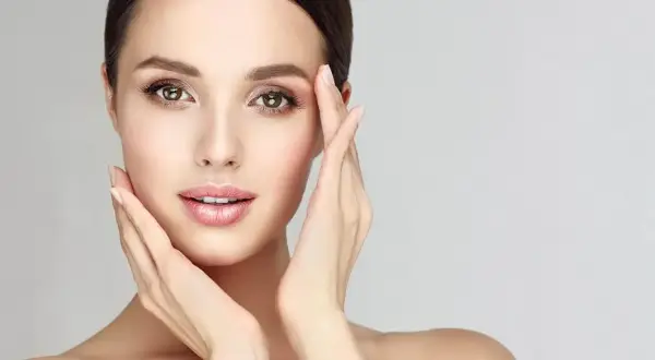Visage de femme aux mains délicates caressant sa peau, évoquant un soin de nettoyage de peau parfait.