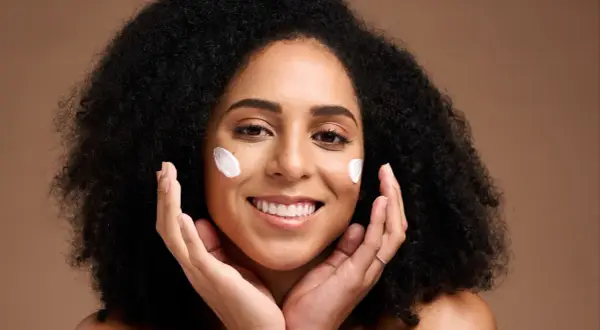 Une femme souriante avec des touches de crème sur les joues, profitant des bienfaits du beurre de karité visage pour une peau douce et hydratée.