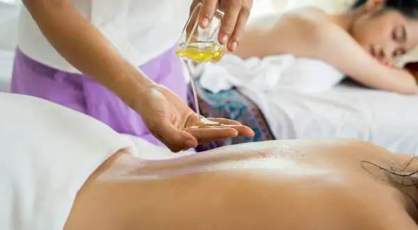 Un massage omoplate relaxant avec de l'huile chaude. Une autre femme se repose sur la table de massage en arrière-plan.