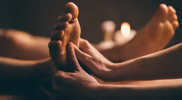 Mains massant un pied, éclairé par des bougies. Une invitation à découvrir ce qu'est la réflexologie plantaire.