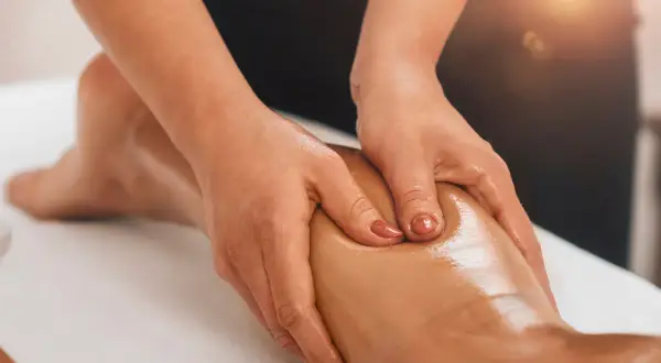 Mains massant un mollet huilé, profitant des bienfaits relaxants et décontractants pour soulager les tensions musculaires.