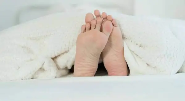 Pieds sous une couverture douillette, prêts pour un point massage pied pour dormir paisiblement.