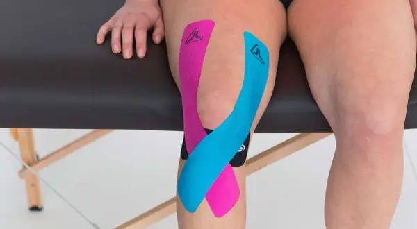 Taping genou arthrose : bandes de kinésiologie rose et bleue appliquées sur un genou pour soulager la douleur.