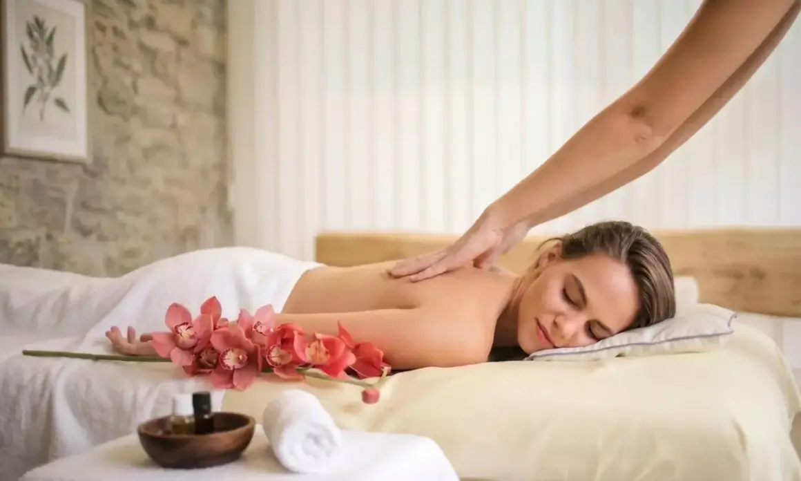 Une femme détendue reçoit un massage du dos, avec des orchidées roses et des huiles de massage à proximité. Offrez-vous un abonnement massage pour un bien-être continu.