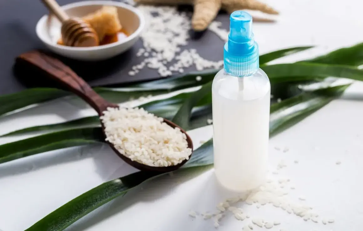 Bouteille de spray remplie d'eau de riz, avec une cuillère de riz et du miel en arrière-plan.