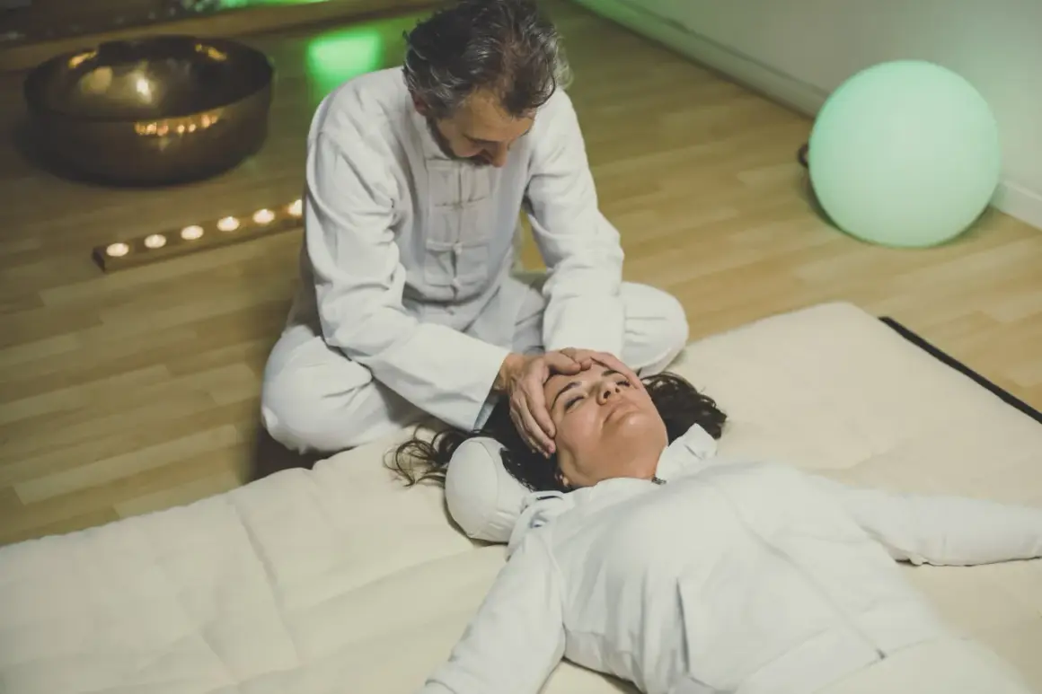 Un praticien effectue un massage japonais shiatsu sur le visage d'une femme allongée, dans une ambiance apaisante avec une lumière verte et des bougies.
