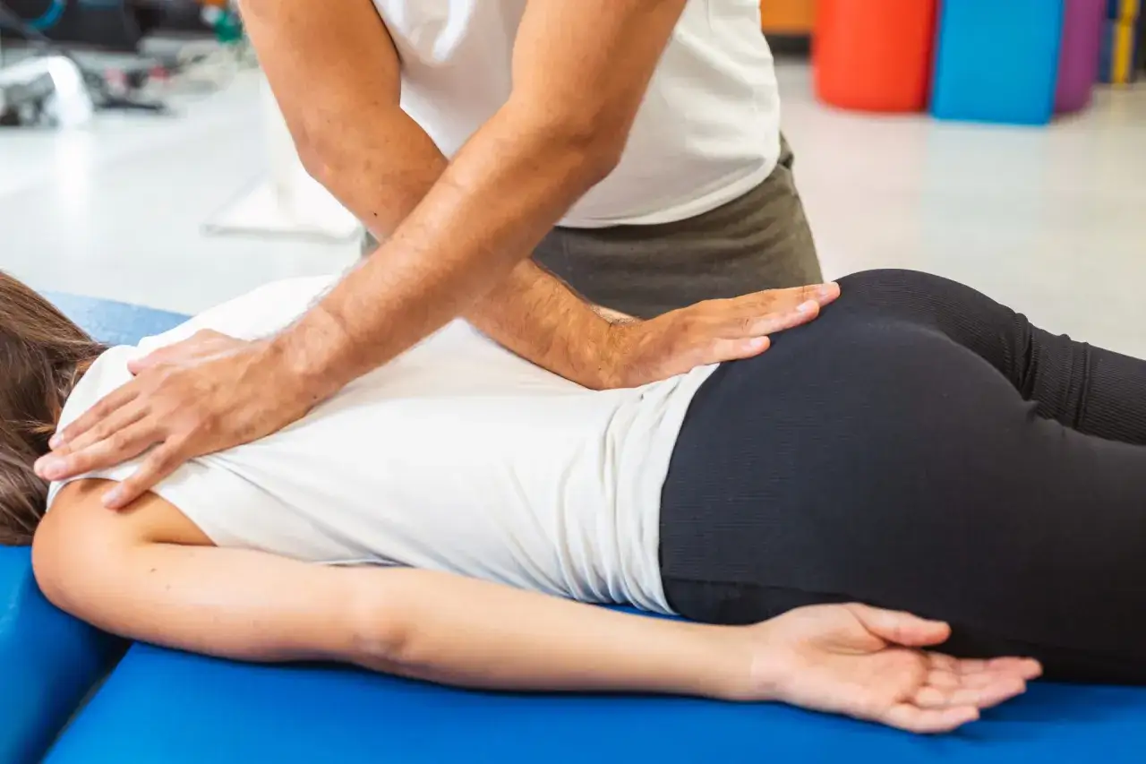 Un thérapeute pratique un massage du nerf sciatique sur une patiente allongée sur une table bleue.
