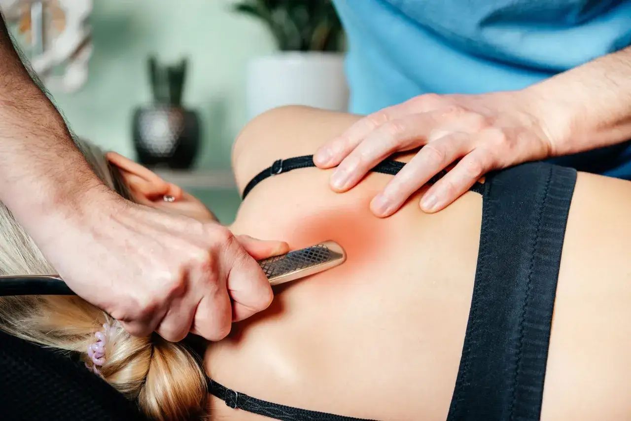 Thérapeute utilisant un outil pour soulager une grosse contracture musculaire dans le dos d'une femme.