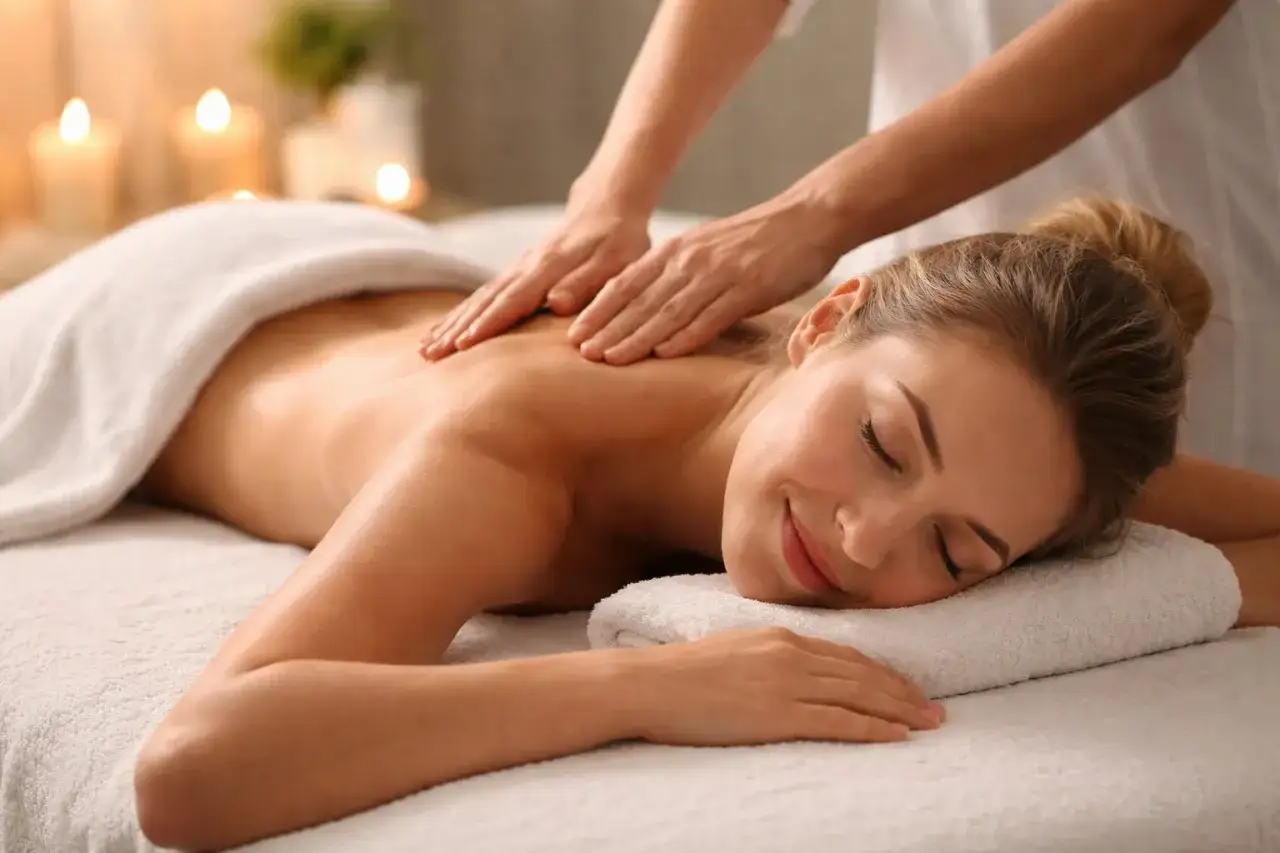 Une femme savoure un moment de massage et relaxation, le visage serein, tandis que des mains expertes lui prodiguent un soin apaisant.