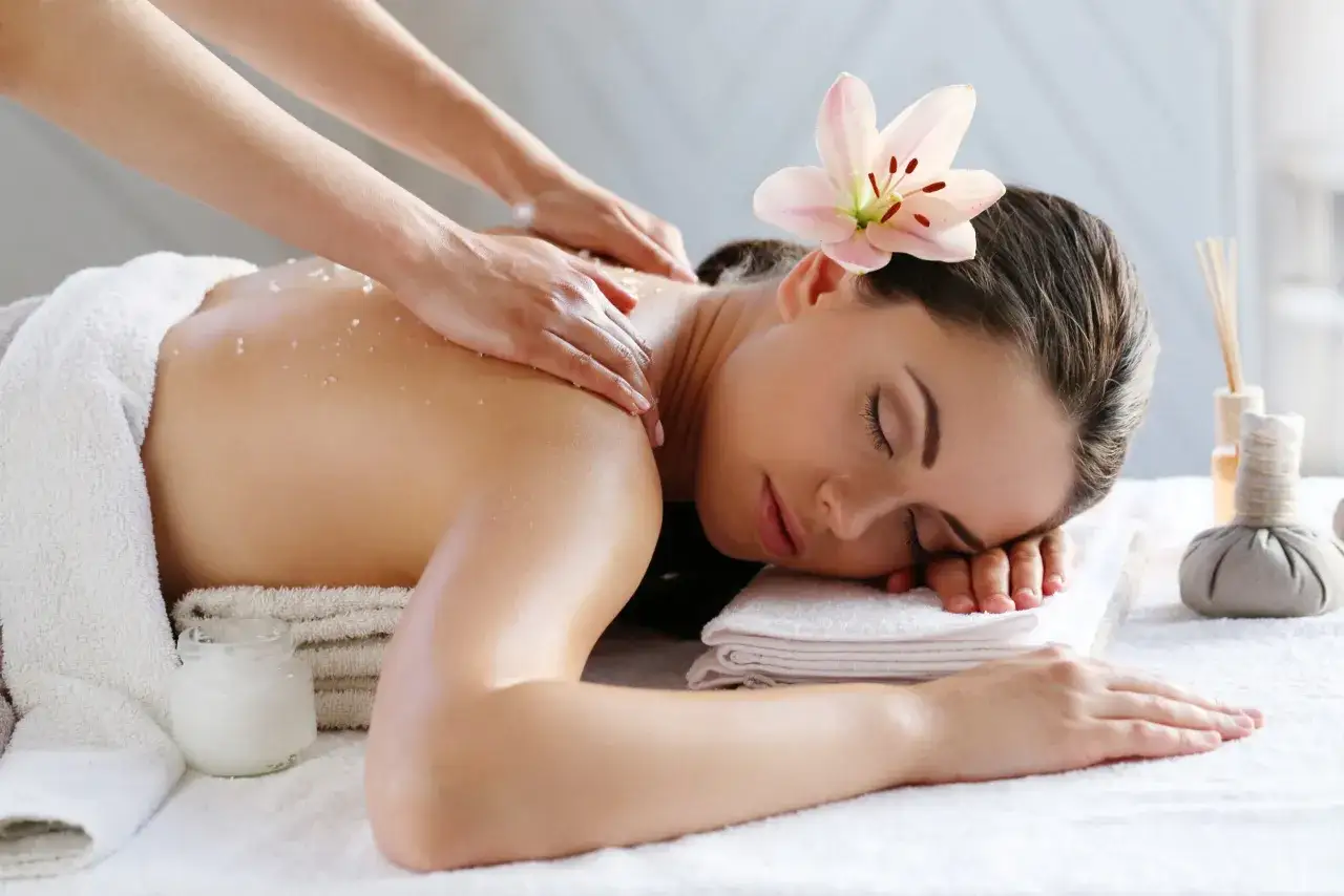 Une femme re&ccedil;oit un massage du dos avec des sels. Une fleur de lys orne ses cheveux. Le massage int&eacute;gral, c'est quoi ? C'est un soin relaxant.