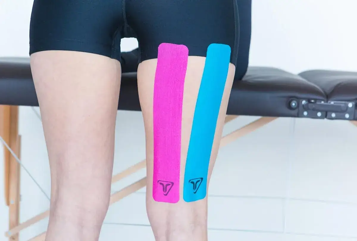 Bandes de kin&eacute;siologie rose et bleue appliqu&eacute;es sur le quadriceps d'une personne, pr&ecirc;tes pour le sport.