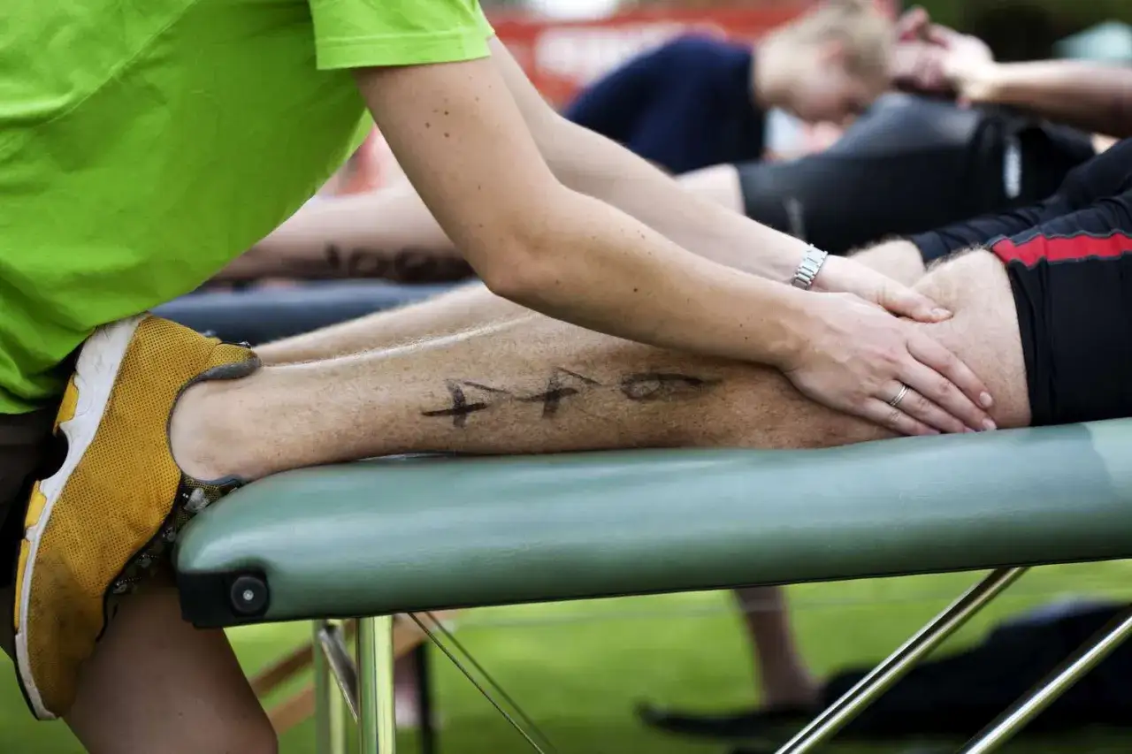 Un athl&egrave;te re&ccedil;oit un massage apr&egrave;s sport sur une table verte. Des marques noires sont visibles sur sa jambe.